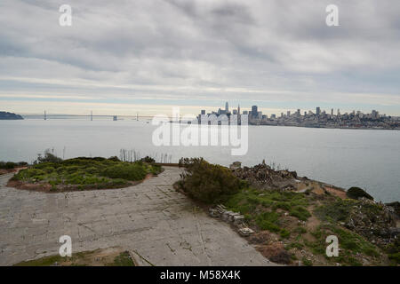 Die San Francisco Skyline gesehen von Alcatraz, der Exerzierplatz und die Ruinen von abgerissenen Gebäuden im Vordergrund. Stockfoto