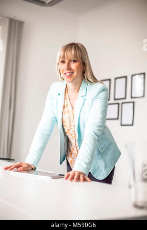 Portrait von selbstbewussten jungen Geschäftsfrau mit Tablet-PC stehen am Tisch im Büro Stockfoto