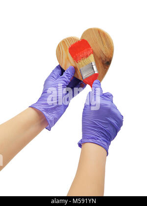 Hand malt die Herzen mit einem Pinsel hand Farbe in rot Holz Herz Hand in blau Handschuh hält ein roter Pinsel Stockfoto