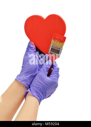 Hand malt die Herzen mit einem Pinsel hand Farbe in rot Holz Herz Hand in blau Handschuh hält ein roter Pinsel Stockfoto
