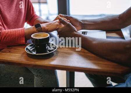 Der Mann und die Frau sitzt an einem Tisch, Hände halten mit einer Tasse Kaffee auf dem Tisch. Zugeschnittenes Bild eines Menschen halten sich an den Händen einer Frau bei einem Kaffee s Stockfoto