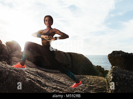 Passen junge Läuferin erstreckt. Junge Frau Stretching im Freien auf Felsen am Strand. Stockfoto