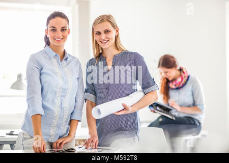 Porträt der glückliche junge Modedesigner mit Kollegin im Hintergrund Stockfoto