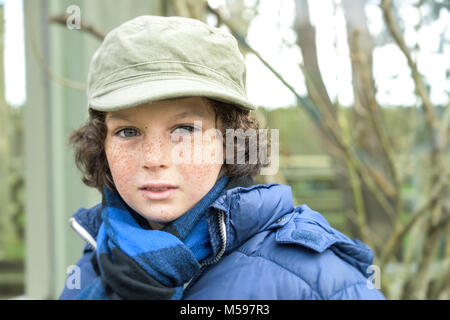 Porträt einer lockigen Haaren kleinen Jungen mit Sommersprossen spielen im Freien an einem Park Stockfoto