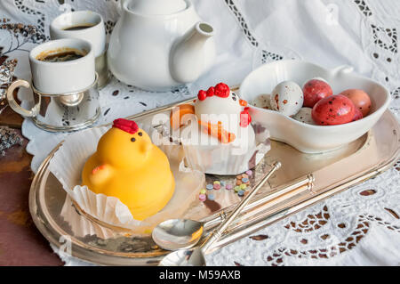 Figuren aus Marzipan in Form von weißen und gelben Hühner auf Ostern Tisch mit Kaffeetassen und Gebäck Eier in einem Ceramic White pot. Close Up. Stockfoto