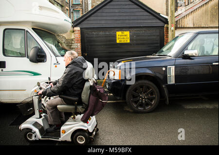 Rücksichtslose Autofahrer UK: ein Mann reitet auf einem Behinderung scooter zwei geparkte Fahrzeuge blockieren den Eintritt in eine private Garage trotz dass das Parken, behinderte Fahrer" zu unterzeichnen. Großbritannien Stockfoto