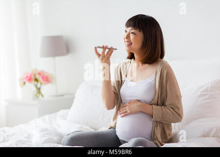 Schwangere Frau mit Voice-Recorder auf smartphone Stockfoto