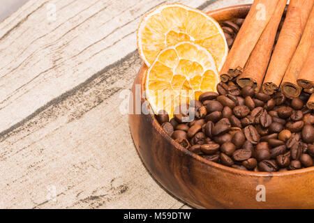 Geröstete Kaffeebohnen mit getrockneten Zitronenscheiben und Zimtstangen in eine hölzerne Schüssel Stockfoto