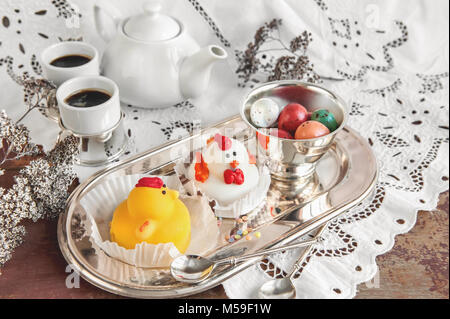 Figuren aus Marzipan in Form von weißen und gelben Hühner auf Ostern Tisch mit Kaffeetassen und Gebäck Eier in einem Ceramic White pot. Close Up. Stockfoto