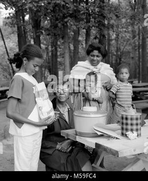 Eine afroamerikanische Familie wird fertig, eine Tasche von State Line Kartoffel Chips auf einer Picknickbank in Neu-England zu genießen, Ca. 1958. Stockfoto