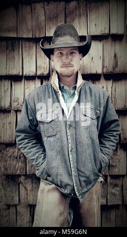 Tausendjährige Cowboy gegen Holz mit Händen in Jeansjacke vergossen Stockfoto