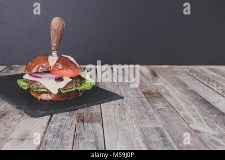 Köstliches Cheeseburger mit Messer auf dunklem Hintergrund Stockfoto