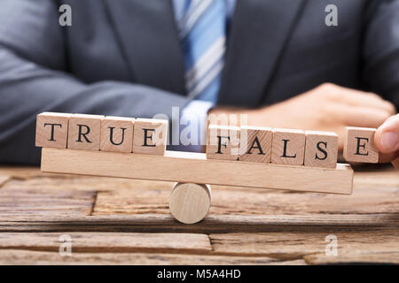 Mittelteil der Geschäftsmann mit true und false Holzklötze auf Wippe am Tisch Stockfoto