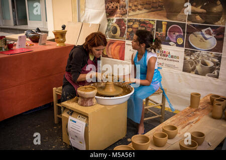 Eine weibliche Potter helfen jungen Mädchen Tontopf auf dem Biegen Rad in behelfsmäßigen keramische Werkstatt am Wochenmarkt in La Bisbal d'Emporda zu machen, Baix Empor Stockfoto