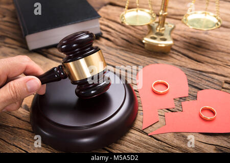 Richter schlagen Mallet durch gebrochene Herz aus Papier mit Ringen und Gerechtigkeit Maßstab auf hölzernen Tisch Stockfoto