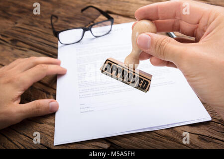 7/8 Hände der Geschäftsmann Holding genehmigt Stempel über Vertrag Papier an den hölzernen Tisch Stockfoto