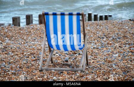 Ein einsamer blau-weiß gestreiften Liegestuhl am Strand in St. Leonards-on-Sea, East Sussex, England. Stockfoto