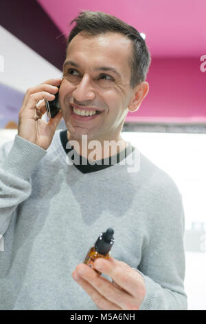 Mann auf Mobiltelefon holding Flasche vaporizer Flüssigkeit Stockfoto