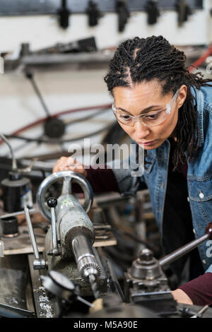 Frau das Tragen von Schutzbrillen, die in der Metallwerkstatt, Arbeiten an einer Maschine. Stockfoto