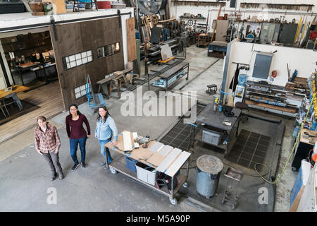 Hohe Betrachtungswinkel von drei Frauen, die in der Metallwerkstatt, an der Kamera schaut. Stockfoto