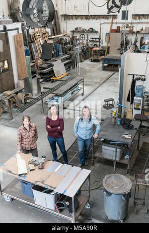 Hohe Betrachtungswinkel von drei Frauen, die in der Metallwerkstatt, an der Kamera schaut. Stockfoto