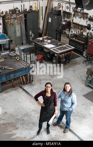 Hohe Betrachtungswinkel von zwei Frauen, die in der Metallwerkstatt, an der Kamera schaut. Stockfoto