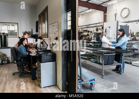 Zwei Frauen an einem Schreibtisch im Büro Bereich einer Metallwerkstatt, Frau, die auf dem mobile Werkbank. Stockfoto