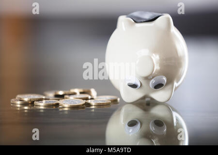 Close-up Sparschwein auf den Kopf in der Nähe von metallischen Münzen auf Schreibtisch Stockfoto