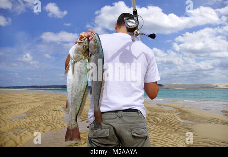 Ein surf Fischer mit zwei großen Seefische auf einer paradiesischen Strand Stockfoto