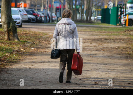 Magdeburg, Deutschland - 21. Februar 2018: Eine ältere Frau geht durch einen Park mit einem roten Koffer, Symbol Bild. Stockfoto