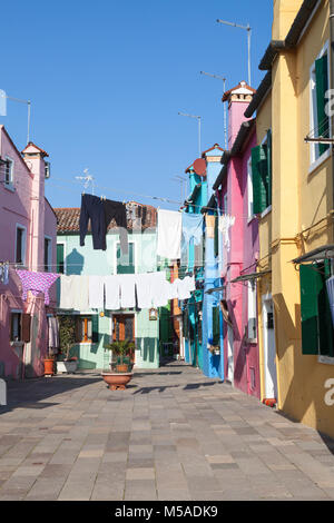 Insel Burano, Venedig, Venetien, Italien. Washday in einem farbenfrohen Calle oder Fußgängerweg mit bunten Häusern gesäumt mit Waschen trocknen im Wint Stockfoto