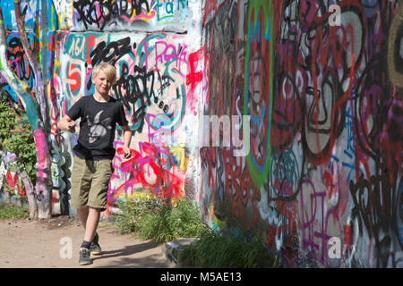 Berlin, Deutschland, 21. Mai - 2017: blonden Jungen männlichen Graffiti Künstler beendete gerade eine Farbenfrohe Wandgemälde Artwork auf der ehemaligen Berliner Mauer am Mauerpark. Stockfoto