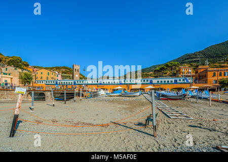 Die Trenitalia Zug fährt durch die Cinque Terre Dorf Monterosso al Mare mit der Stadt einschließlich der Kirche Glockenturm und den Sandstrand Stockfoto