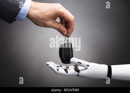 Nahaufnahme der Kaufmann Hand die Autoschlüssel an Roboter auf grauem Hintergrund Stockfoto