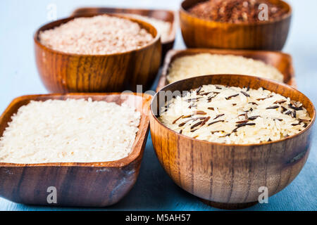 Sechs Schüsseln mit verschiedenen Sorten von Reis auf einer hölzernen Hintergrund. Zutaten für eine gesunde Ernährung. Stockfoto