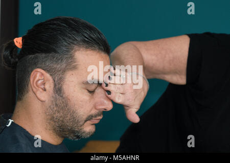 Weibliche friseur Reinigung Gesicht des jungen Mannes mit der Hand nach dem rasieren die Haare Stockfoto