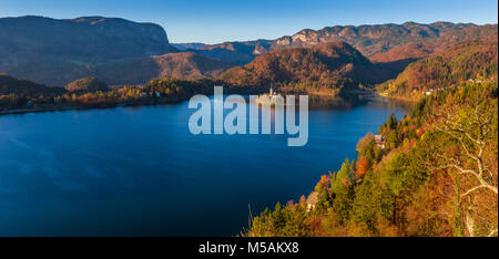 Bled, Slowenien - Panoramablick auf die Skyline Blick auf den Bleder See mit warmen Herbst Laub und die berühmte Wallfahrtskirche Mariä Himmelfahrt der Maria und die Alpen. Stockfoto