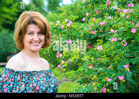 Porträt der schönen Frau, die auf dem Hintergrund einer blühenden Wild Rose Stockfoto