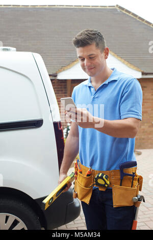 Builder mit Van Kontrolle SMS auf Handy ausserhalb des Hauses Stockfoto