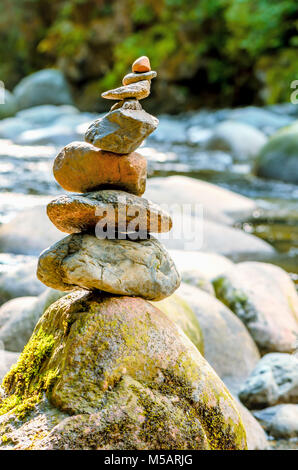 Die Menschen gemachte Stapel oder Stack von Steinen mit grünen moh namens Cairn auf der banch des Flusses zwischen anderen Steinen und grünen Pflanzen entfernt Stockfoto