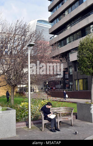 Ein Mann essen sein Mittagessen auf einer Bank während seiner Mahlzeit Pause in der Stadt London unter den hohen Bürogebäuden der Stadt London und finanziellen Bereich. Stockfoto