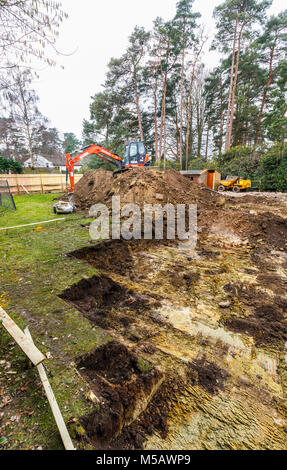 Große orange schwere Anlage mechanische Bagger auf einer Erde Hügel geparkt nach graben Ausgrabungen für die Grundlagen einer neuen Wohnanlage Stockfoto