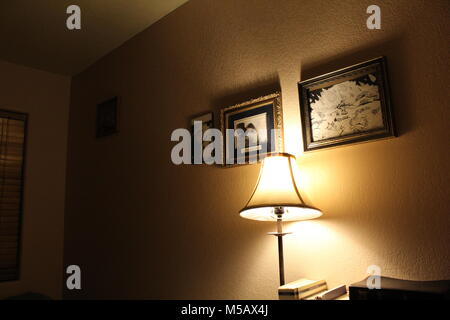 Ein ruhiges Zimmer beleuchtet durch eine kleine Lampe mit Fotografien an der Wand erzeugen eine ruhige Atmosphäre am Abend hing. Stockfoto