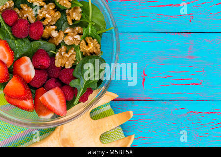 Frische baby Spinatsalat mit Himbeeren und Erdbeeren und ohne Schale Walnüsse in der Schale serviert auf einer exotischen blau Crackle Paint Holz Hintergrund mit c Stockfoto