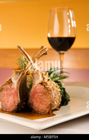 Rack mit Lammkoteletts Rippen auf Knochen aufrecht vergoldet, grünes Gemüse, Rotwein im Restaurant, Vertikal, Abdeckung, Portraitfotos text Platz auf Seiten Stockfoto