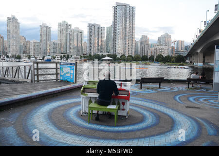 Ein Mann spielt ein Klavier im Freien an einem öffentlichen Platz neben False Creek und die Cambie Street Bridge in der Innenstadt von Vancouver, British Columbia, Kanada. Stockfoto