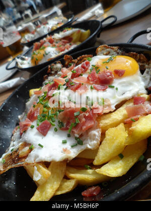 Ein Gericht der Fried Potato Chips/Pommes frites garniert mit Spiegelei, Speck und frischen gehackten Schnittlauch in eine Spanische Tapas Bar, Fuengirola, Spanien serviert. Stockfoto