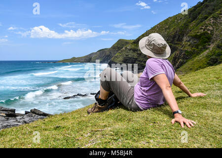 Eine weibliche Wanderer im Fokus sitzen, genießen Sie die Aussicht auf die Küste auf den Spuren von Coffee Bay am Indischen Ozean in der Eastern Cape im Wild Co Stockfoto
