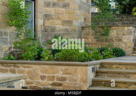 Kleine Ecke des schönen, gepflegten, privaten Garten mit zeitgenössischem Design, gepflasterte Stufen, Grenze Sträucher und Pflanzen durch Haus-Yorkshire, England, UK. Stockfoto