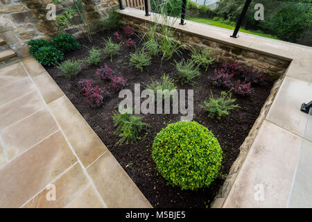 Kleine Ecke des schönen, gepflegten, privaten Garten mit zeitgenössischem Design, gepflasterte Terrasse & frisch Grenze Sträucher & Pflanzen - Yorkshire, England, UK. Stockfoto